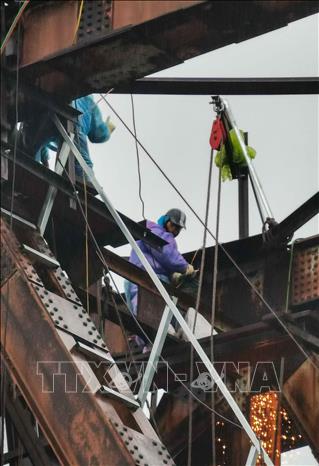 Không quản ngại mưa rét, công nhân làm việc liên tục tại khu vực nhịp cầu, triển khai phương án sửa chữa, gia cố kết cấu thép. Ảnh: Thanh Tùng - TTXVN