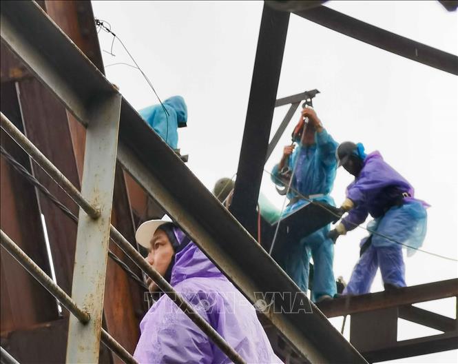 Không quản ngại mưa rét, công nhân làm việc liên tục tại khu vực nhịp cầu, triển khai phương án sửa chữa, gia cố kết cấu thép. Ảnh: Thanh Tùng - TTXVN
