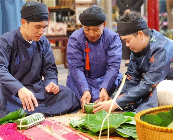 Trong trang phục áo dài truyền thống, cùng bên nhau gói bánh chưng đón Tết cổ truyền. Ảnh: Thanh Tùng – TTXVN