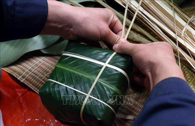 Những đôi bàn tay vốn quen cầm bình chữa cháy, leo thang cứu nạn nay lại khéo léo xếp lá, đong gạo, gói từng chiếc bánh chưng. Ảnh: Phạm Kiên - TTXVN