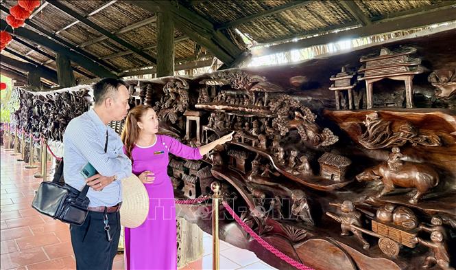 Du khách tham quan bức tranh gỗ lũa khổng lồ dài gần 25 m, nặng khoảng 20 tấn, được xem là một trong những tác phẩm công phu bậc nhất Việt Nam. Ảnh: Thanh Sang-TTXVN