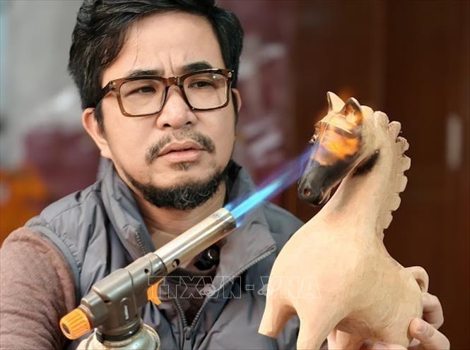 Nghệ nhân ưu tú Nguyễn Tấn Phát đang thực hiện công đoạn khò cháy. Ảnh: Quốc Lũy - TTXVN