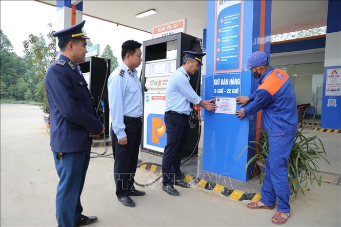 Cán bộ Đội Quản lý thị trường dán số 7 niêm yết số điện thoại đường dây nóng tại cửa hàng xăng dầu, tiếp nhận phản ánh của người dân trong bối cảnh giá xăng tăng cao kỷ lục. Ảnh: Khiếu Tư - TTXVN