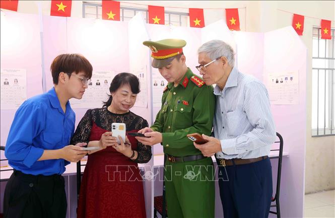 Cán bộ, chiến sĩ Công an phường Ngọc Hà hướng dẫn cử tri tra cứu thông tin và thay đổi khu vực bỏ phiếu trên ứng dụng VNeID. Ảnh: Phạm Kiên - TTXVN