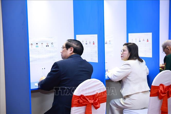 Thủ tướng Phạm Minh Chính và Phu nhân tìm hiểu tiểu sử người ứng cử tại Khu vực bỏ phiếu số 21 phường Tây Hồ, thành phố Hà Nội. Ảnh: Dương Giang-TTXVN 
