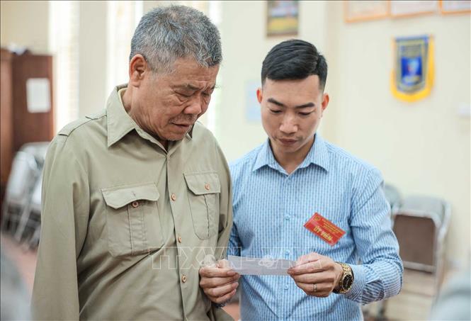 Cử tri Nguyễn Văn Đáp (thương binh có tỉ lệ thương tật 81%, mất cả 2 tay) được thành viên Tổ bầu cử hỗ trợ tại điểm bỏ phiếu. Ảnh: Hoàng Hiếu - TTXVN 