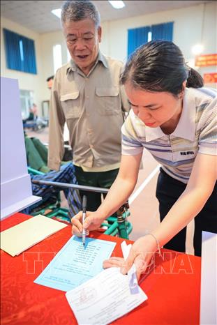 Bác sĩ Phạm Thị Pha - Phó trưởng phòng y tế Trung tâm Điều dưỡng thương binh Thuận Thành hỗ trợ thương binh Nguyễn Văn Đáp (thương binh có tỉ lệ thương tật 81%, mất cả 2 tay) bỏ phiếu. Ảnh: Hoàng Hiếu - TTXVN