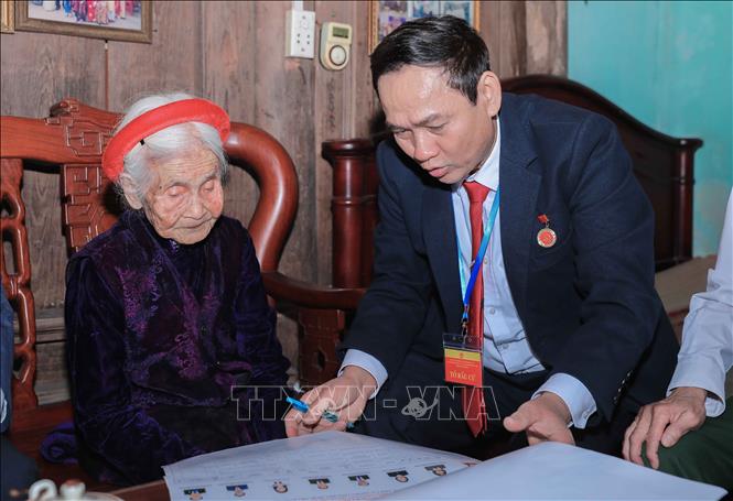 Cán bộ phường Phúc Lợi trực tiếp hỗ trợ, giới thiệu danh sách người ứng cử cho cử tri Chu Thị Nhớn, 102 tuổi, cử tri cao tuổi thuộc gia đình có công với cách mạng. Ảnh: Phan Phương – TTXVN