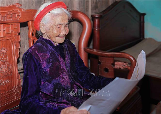 Cán bộ phường Phúc Lợi trực tiếp hỗ trợ, giới thiệu danh sách người ứng cử cho cử tri Chu Thị Nhớn, 102 tuổi, cử tri cao tuổi thuộc gia đình có công với cách mạng. Ảnh: Phan Phương – TTXVN