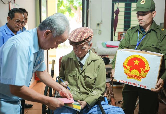 Thành viên tổ bầu cử đưa phiếu bầu đến cho cử tri Mai Văn Mỳ sinh năm 1948, thương binh hạng ¼, tỷ lệ thương tật 91% ). Ảnh: Hoàng Hiếu - TTXVN 