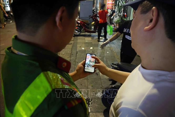 Cán bộ, chiến sĩ Công an phường Hoàn Kiếm cung cấp hình ảnh chứng minh vi phạm trật tự đô thị cho chủ cơ sở kinh doanh tại phố Nguyễn Siêu. Ảnh: Phạm Kiên - TTXVN