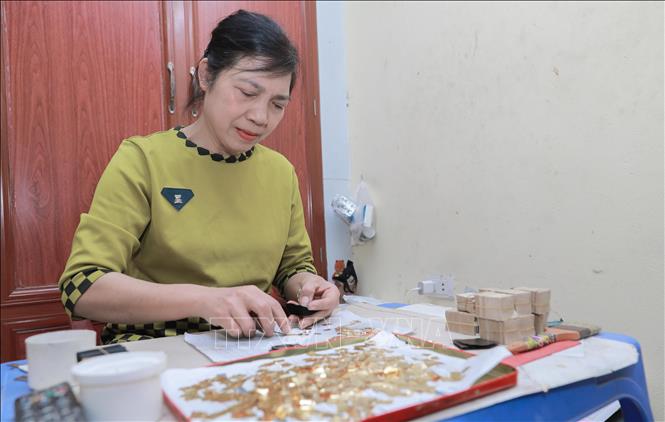 Nghệ nhân Nguyễn Thị Bích Thủy, gia đình có ba thế hệ làm nghề, thực hiện lồng quỳ và trại quỳ. Đây la công đoạn đòi hỏi sự kiên nhẫn, tỉ mỉ tuyệt đối để tạo ra những lá vàng mỏng, tinh khiết. Ảnh: Phan Phương – TTXVN
