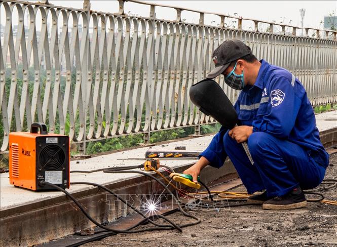 Đơn vị thi công triển khai hàn lắp hệ thống máng thoát nước mới dọc theo mặt cầu, đảm bảo khả năng tiêu thoát nước sau khi hoàn thiện. Ảnh: Vân Chi/TTXVN phát
