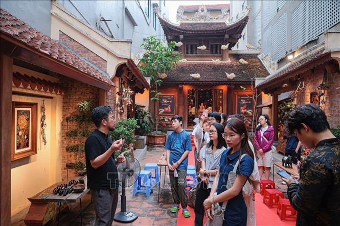 Khách tham gia lắng nghe nghệ nhân Nguyễn Tấn Phát chia sẻ về kỹ thuật và ý nghĩa của các tác phẩm sơn mài trong không gian đình cổ. Ảnh: Phạm Tuấn Anh - TTXVN
