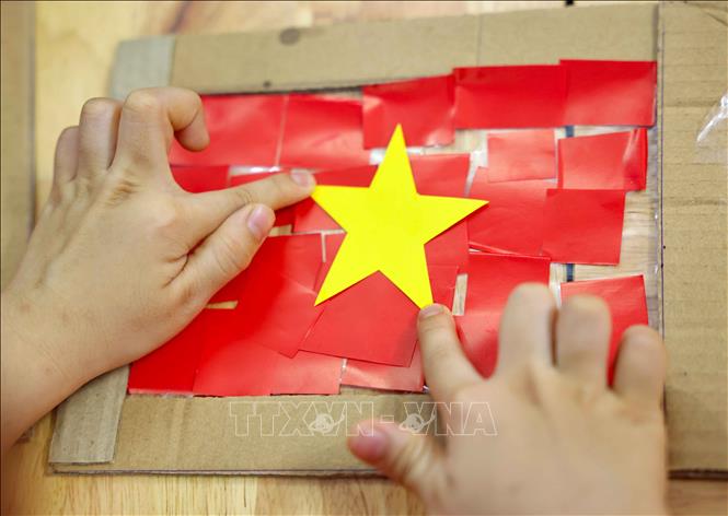 Trẻ tỉ mỉ, chăm chút cắt dán thành lá cờ Tổ quốc yêu thương và rực rỡ. Ảnh: Thanh Tùng - TTXVN  