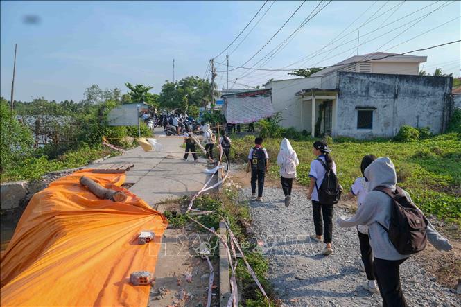 Các em học sinh ở ấp Phú Tây, xã Nhơn Mỹ đi học ngang qua đoạn sạt lở bờ sông Phụng An làm sụp tuyến đường giao thông ven sông. Ảnh: Thanh Liêm - TTXVN