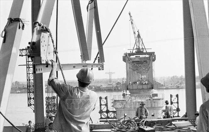 Cùng với lịch sử và sự phát triển của đất nước có những công trình mang đậm dấu ấn trí thức Việt trong lĩnh vực nghiên cứu ứng dụng, có những công trình là kết tinh trí tuệ, bản lĩnh và công sức của tập thể những người lao động Việt Nam để cống hiến âm thầm cho cộng đồng. Trong ảnh: Công nhân đội lắp dầm thép 112, công ty cầu 11 khẩn trương lắp những khoang cầu cuối cùng của cầu Thăng Long (1984). Ảnh: Chu Chí Thành - TTXVN