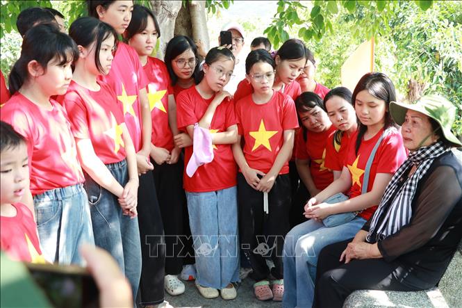 Học sinh lắng nghe bà Phạm Thị Hường (trú phường Đông Ninh Hòa), nhân viên hậu cần bến Hòn Hèo kể về những câu chuyện lịch sử, sự hy sinh anh dũng của các chiến sĩ và Tàu C235 năm 1968. Ảnh: Phan Sáu - TTXVN