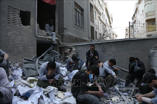 Người dân Iran bên những toà nhà đổ nát sau các cuộc không kích của Mỹ và Israel xuống thủ đô Tehran ngày 15/3/2026. Ảnh: THX/TTXVN