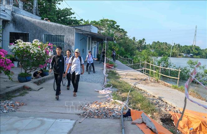 Học sinh xã Nhơn Mỹ đi học trên con đường tạm (trước đây là nhà dân) sau khi tuyến đường chính bị sụp xuống sông. Ảnh: Thanh Liêm - TTXVN