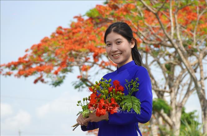 A young girl poses for a photo with phuong vi flowers. VNA Photo: Nhựt An