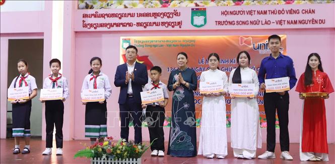 The Principal of Nguyen Du Laos-Vietnam Bilingual School and the Director of Unite Company present scholarships to disadvantaged students with outstanding academic achievements. VNA Photo: Xuân Tú