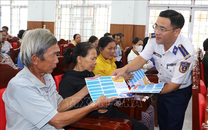 Cảnh sát biển phát tờ rơi tuyên truyền chống khai thác bất hợp pháp cho bà con ngư dân. Ảnh: Đinh Hương - TTXVN