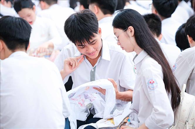Giữa sân trường đông đúc ngày bế giảng, học sinh chuyền tay nhau từng chiếc áo để viết lời nhắn trước giờ chia tay. Ảnh: Phạm Tuấn Anh - TTXVN