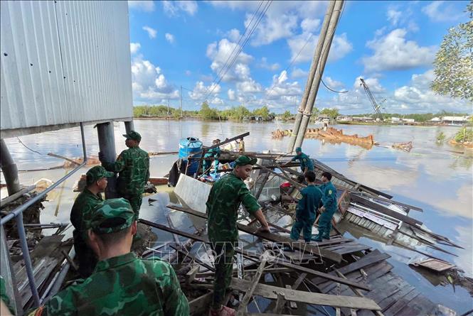 Cán bộ chiến sĩ Đồn Biên phòng Năm Căn (Cà Mau) hỗ trợ các hộ dân di dời tài sản sau sạt lở. Ảnh: TTXVN phát.