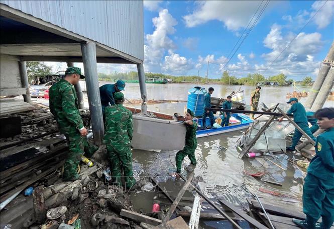 Cán bộ chiến sĩ Đồn Biên phòng Năm Căn (Cà Mau) hỗ trợ các hộ dân di dời tài sản sau sạt lở. Ảnh: TTXVN phát.