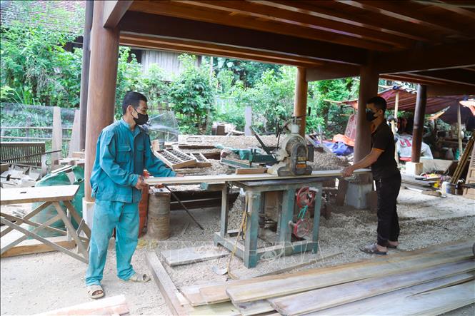 Người dân bản Na Cọ (xã Bình Chuẩn) dùng máy móc và hỗ trợ giúp nhau cưa xẻ gỗ, thưng ván làm nhà sàn truyền thống. Ảnh: Xuân Tiến - TTXVN 