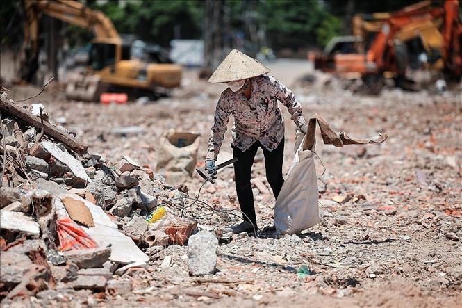 Một phụ nữ thu gom phế liệu giữa bãi đất, công trình ngổn ngang dưới nền nhiệt cao. Ảnh: Phạm Tuấn Anh - TTXVN
