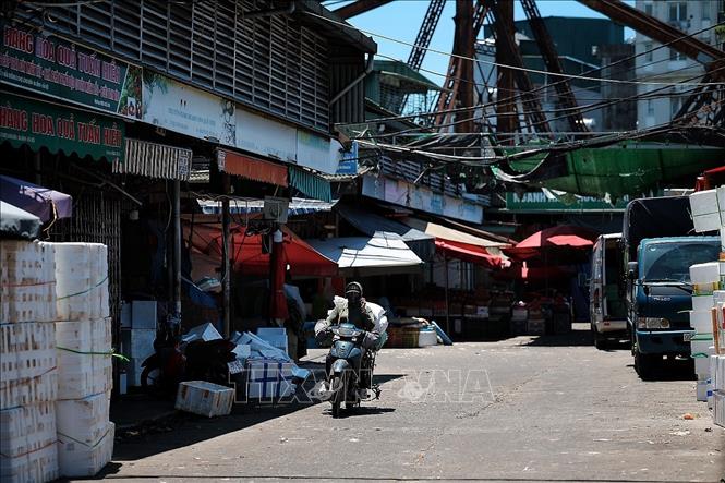 Người lao động di chuyển qua khu vực chợ đầu mối trong khung giờ nắng gắt, khi nhiều tuyến phố gần như vắng bóng người đi bộ. Ảnh: Phạm Tuấn Anh - TTXVN