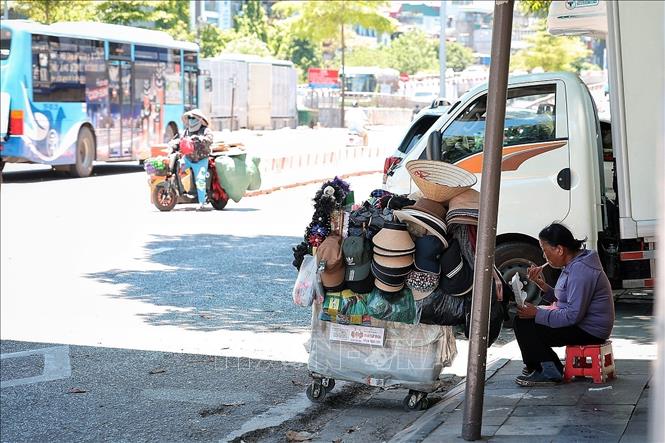 Một người bán hàng rong tranh thủ ngồi nghỉ, ăn vội bữa trưa bên vỉa hè dưới cái nắng gay gắt giữa Hà Nội ngày 25/5. Ảnh: Phạm Tuấn Anh - TTXVN