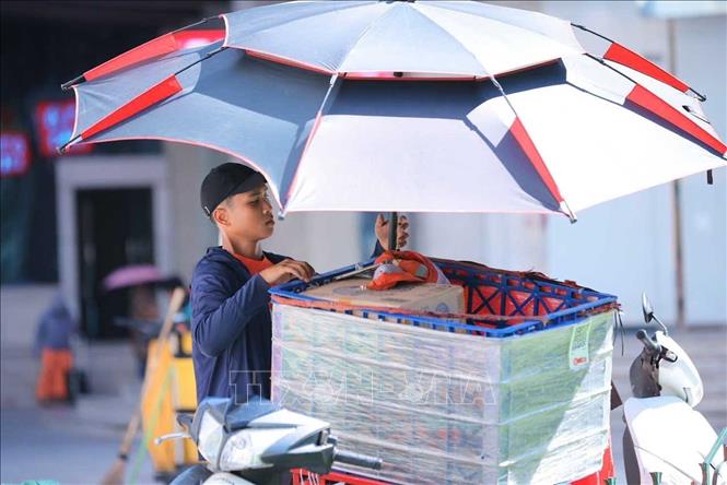 Người giao hàng phải tìm cách chống nắng khi nhiệt độ ngoài trời tăng cao. Ảnh: Hoàng Hiếu - TTXVN