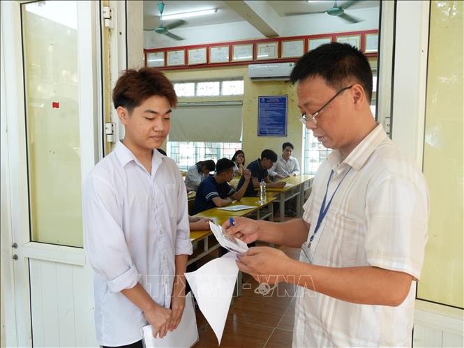Giám thị tại điểm thi Trường THPT Vĩnh Yên kiểm tra thông tin của thí sinh trước khi vào phòng thi. Ảnh: Nguyễn Thảo - TTXVN