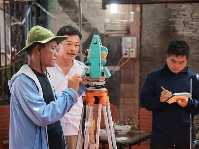 Nhân viên đo đạc sử dụng máy toàn đạc để xác định mốc, thu thập số liệu hiện trạng tại các hộ dân số 1 Đào Duy Anh, tổ 75, phường Kim Liên. Ảnh: Hoàng Hiếu - TTXVN