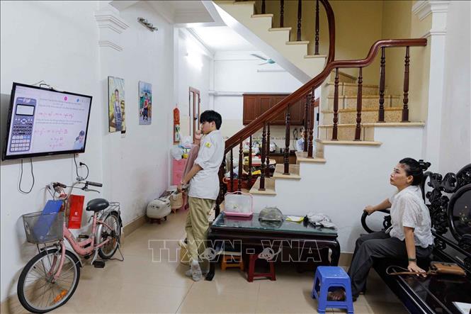 Trước kỳ thi, sĩ tử tranh thủ tham khảo thêm cái bài giảng trực tuyến. Phía sau là sự đồng hành thầm lặng của người mẹ. Ảnh: Phạm Tuấn Anh - TTXVN
