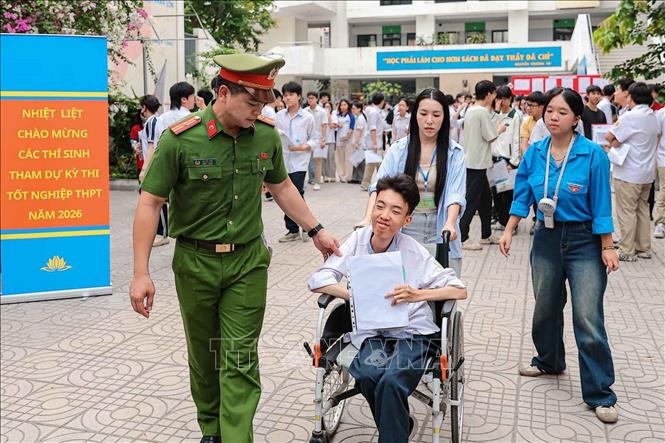 Công an phường Ô Chợ Dừa và tình nguyện viên hỗ trợ Sơn di chuyển bằng xe lăn tại điểm thi. Ảnh: Phạm Tuấn Anh - TTXVN