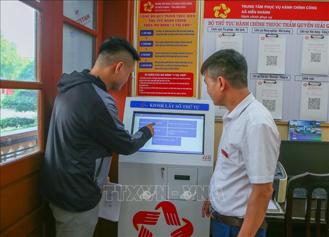 Cán bộ Trung tâm Phục vụ hành chính công xã Hiển Khánh hướng dẫn người dân lấy số thứ tự. Ảnh: Công Luật - TTXVN