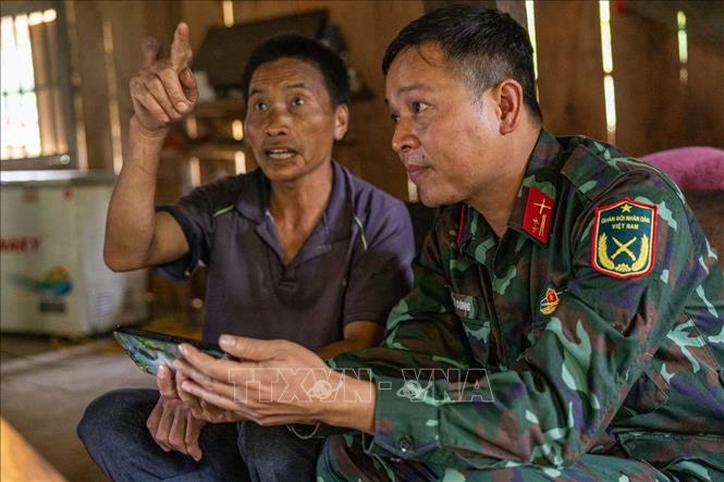 Trung tá Hoàng Vũ Dũng trao đổi, xác minh thông tin được cung cấp với ông Vàng Xeo Phù - Chủ tịch MTTQ Thôn Hoàng Đình Phả - người sống gần địa điểm nghi mộ phần 12 liệt sĩ. Ảnh: Hoàng Hiếu - TTXVN