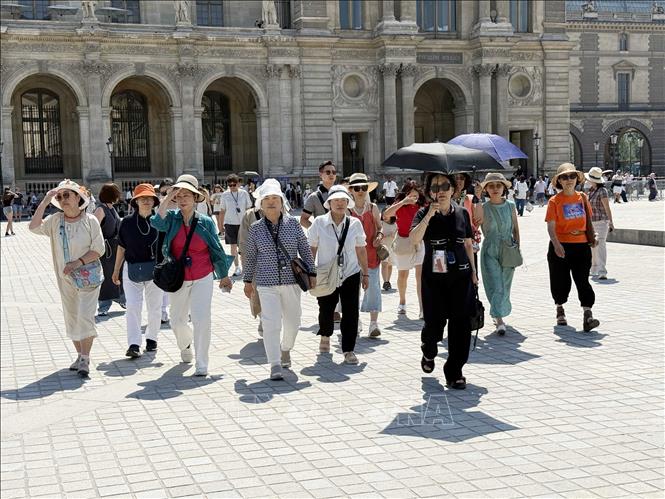 Du khách đội mũ, che ô và tìm cách chống nắng khi tham quan bảo tàng Louvre ở thủ đô Paris. Ảnh: Hữu Chiến - PV TTXVN tại Pháp
