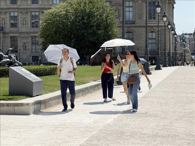 Người dân và du khách sử dụng ô để tránh nắng khi tham quan khu vực bảo tàng Louvre ở thủ đô Paris trong ngày nắng nóng. Ảnh: Hữu Chiến - PV TTXVN tại Pháp