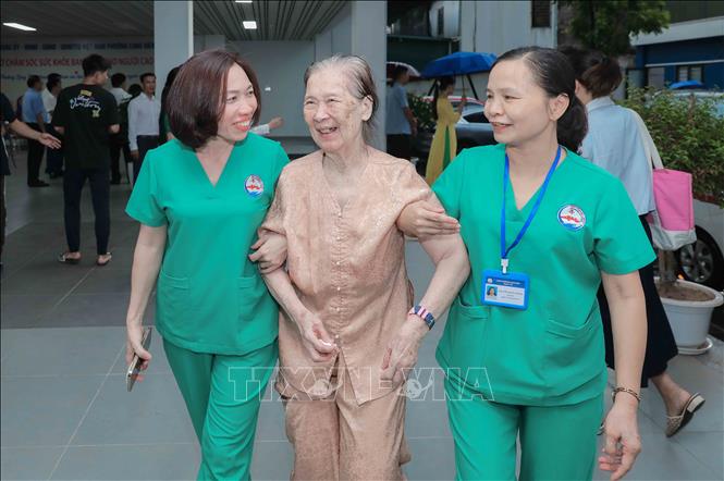 Cụ Vũ Thị Tuấn (86 tuổi) rất phấn khởi khi được người nhà đưa đến và hẹn chiều đón. Cụ được nhân viên y tế hỗ trợ di chuyển để kiểm tra sức khỏe trước khi vào phòng sinh hoạt chung. Ảnh: Phan Phương – TTXVN