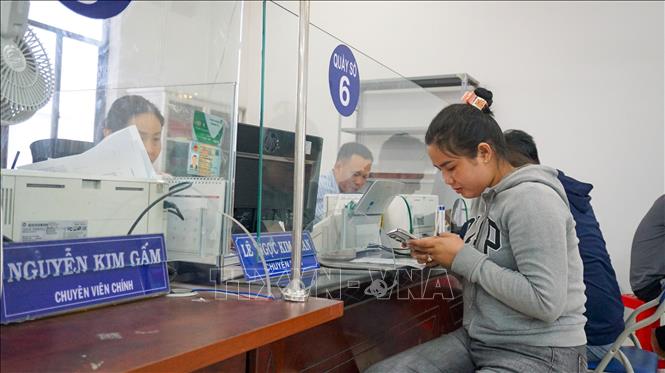 Người dân sử dụng điện thoại thông minh để thực hiện các thủ tục hành chính trực tuyến dưới sự hỗ trợ của cán bộ tại Trung tâm Phục vụ hành chính công phường Long Hoa, tỉnh Tây Ninh. Ảnh: Minh Phú – TTXVN