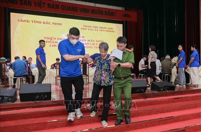Lực lượng Công an xã Yên Phong phối hợp cùng các tình nguyện viên tích cực đồng hành, hỗ trợ các cụ là thân nhân liệt sĩ trong quá trình di chuyển và thực hiện thủ tục lấy mẫu ADN. Ảnh: Phan Phương-TTXVN