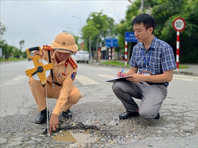 Cán bộ Đội Cảnh sát giao thông đường bộ số 15 (Phòng Cảnh sát giao thông Hà Nội) kiểm tra hiện trạng mặt đường Lê Hữu Tựu, ghi nhận các vị trí bong tróc, hư hỏng mặt đường trong quá trình khảo sát thực tế. Ảnh: Trung Nguyên - TTXVN