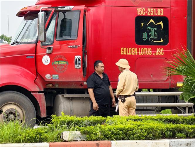 Cán bộ Đội Cảnh sát giao thông đường bộ số 15 (Phòng Cảnh sát giao thông Hà Nội) tuyên truyền, hướng dẫn lái xe chấp hành quy định về tải trọng và lộ trình lưu thông đối với phương tiện ra, vào khu công nghiệp Nguyên Khê. Ảnh: Trung Nguyên - TTXVN