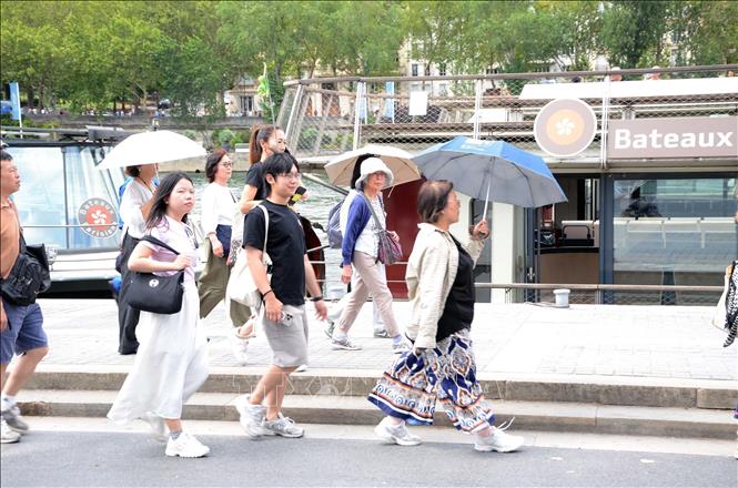 Người dân và du khách sử dụng ô che nắng khi đi bộ dọc khu vực ven sông Seine ở thủ đô Paris, ngày 14/7/2026. Ảnh: Hữu Chiến - PV TTXVN tại Pháp