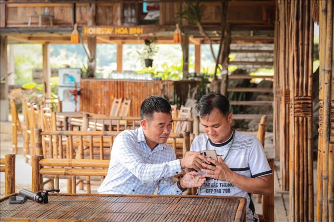 Đồng chí Nguyễn Duy Tư, Bí thư Đảng ủy xã Vân Sơn, tỉnh Phú Thọ hướng dẫn chủ homestay sử dụng điện thoại để ghi hình, giới thiệu không gian lưu trú, các dịch vụ và những nét đặc trưng của cơ sở trên nền tảng số. Ảnh: Phạm Tuấn Anh - TTXVN